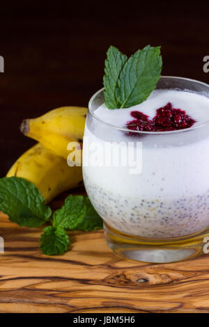 Nahaufnahme eines Glases mit Banane Chia Samen Pudding Schichten mit einem rohe Kokosmilch Joghurt mit einem Klacks pürierte Beeren an der Spitze Stockfoto