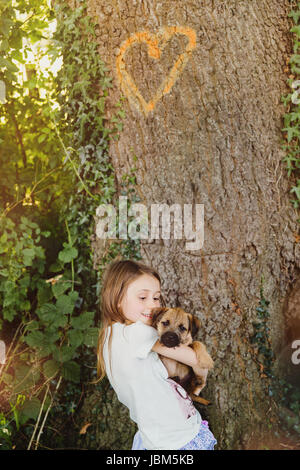 Mädchen hält Hündchen unter Baum mit Herz-Form Stockfoto