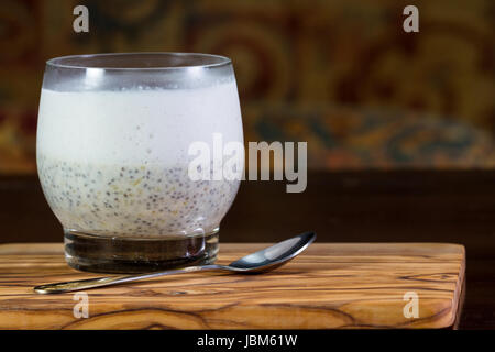 Nahaufnahme eines Glases mit Banane Chia Samen Pudding Schichten mit einem rohe Kokosmilch Joghurt mit einem Klacks pürierte Beeren an der Spitze Stockfoto