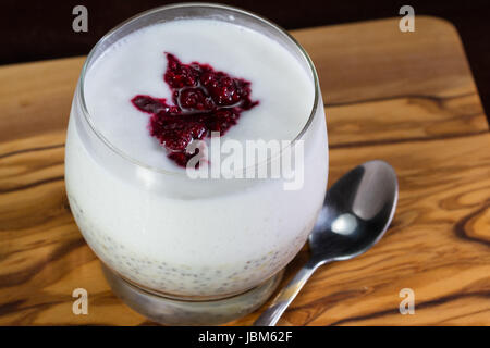 Nahaufnahme eines Glases mit Banane Chia Samen Pudding Schichten mit einem rohe Kokosmilch Joghurt mit einem Klacks pürierte Beeren an der Spitze Stockfoto