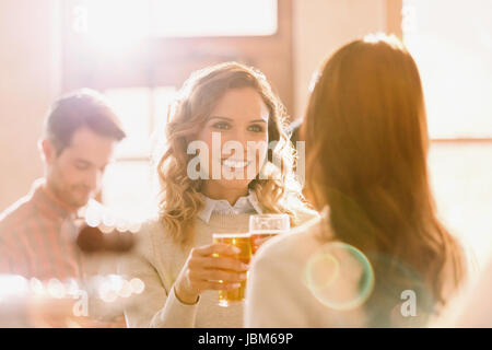 Lächelnde Frauen Freunde Gläser Toasten Bier im sonnigen bar Stockfoto