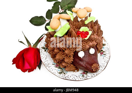 Kuchen in der Form eines Igels, geschmückt mit grünen Blättern mit Sahne, Pilze aus Biskuit und Baiser, Beeren, Gelee auf einen Teller mit einer roten rose Knospe Stockfoto