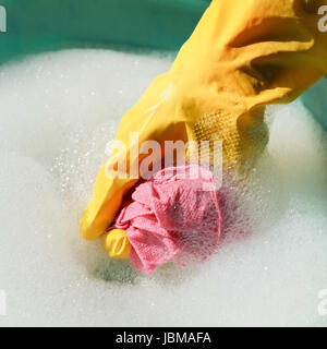 Hand im gelben Gummihandschuh nassen Duster in Seifenwasser spülen Stockfoto