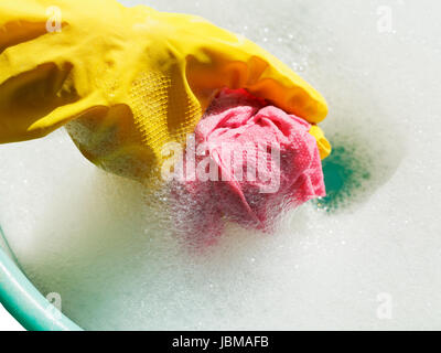 Hand im gelben Gummihandschuh Lappen in Seifenlauge Seifenwasser spülen Stockfoto