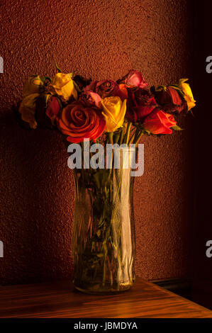 Bunte Rosen in Glasvase mit warmen Fenster Fensterlicht welke Stockfoto