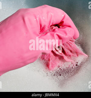 Hand in rosa Gummihandschuh ringt, nasses Tuch aus dem schäumenden Wasser Stockfoto