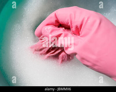 Hand in rosa Gummihandschuh nasses Tuch im schäumenden Wasser spülen Stockfoto