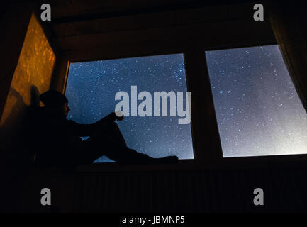 Mann sitzt im Fenster in der Nacht Stockfoto