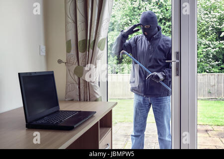 Dieb bricht in ein Haus über eine Terrasse Türen Fenster mit einem Brecheisen, einen Laptop-Computer von einem Schreibtisch zu stehlen Stockfoto