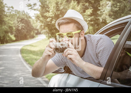 Porträt des jungen begeistert Touristen Kerl durch das Fenster vom Fahrersitz auf Straße Reise Reisen Urlaub mit Vintage-retro-Kamera fotografieren. Stockfoto