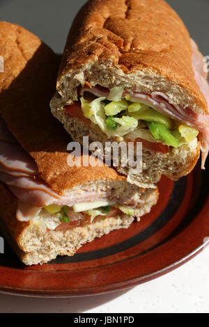 Ein Hoagie oder u-Boot Aufschnitt Sandwich halbiert und auf einem braunen Platte in natürlichem Licht gelegt. Stockfoto