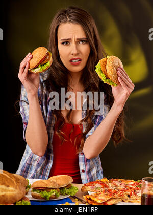 Aufgeregt Mädchen halten große zwei kleine Hamburger und Pizza. Fastfood-Konzept auf grünem Hintergrund. Weibchen ist traurig über mangelnde Ernährung. Stockfoto