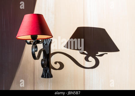 Eine rote Wand Lampe mit seinem Schatten. Es ist ein Objekt, die verwendet wird, um auf das Licht mit elektrischem Strom zu drehen.