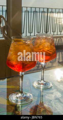 Kellner vorbereitet Aperol Sprits Sommer cocktail mit Aperol, prosecco, Eis-Würfel und Orange im Weinglas, bereit, auf der sonnigen Terrasse mit Meer zu trinken Stockfoto