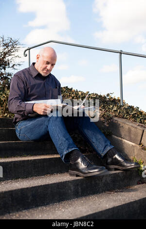 Mann Mittleren Alters, Senior Sitz Mit Einer Zeitung Auf Einer Treppe Im Frühling Im Freien Stockfoto