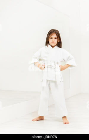 In voller Länge Portrait von Karate Mädchen in weißen Kimono ansehen mit Hände auf den Hüften in leichte Fitness-Studio Stockfoto