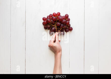 Des Mädchens Hand hält eine Reihe von roten Trauben auf einem hölzernen Hintergrund an. Ansicht von oben. Trauben sind wie Luftballons Stockfoto