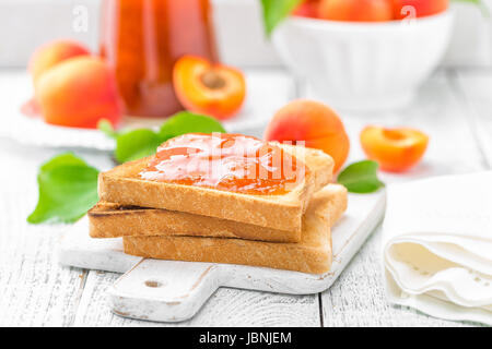 Toast Brot mit Marillenmarmelade und frisches Obst mit Blättern auf weißer Holztisch. Leckeres Frühstück. Stockfoto
