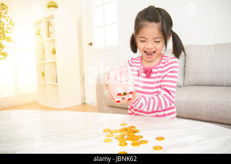 niedliche kleine asiatische Mädchen aufgeregt, um leere Gießen ihr Sparschwein nachdem es voll Geld einzahlen, im Wohnzimmer zu Hause. Familientätigkeit Konzept. Stockfoto