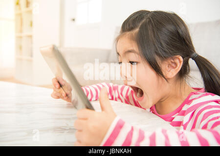 schockiert überrascht Pre Teen Mädchen spielen auf TabletPC geöffnet Mund im Wohnzimmer zu Hause. Familientätigkeit Konzept. Stockfoto