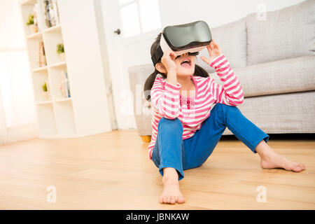 Lebensstil Schuss ein Staunen kleines Kind mit einer virtual-Reality Brille mit offenem Mund schockiert auf Holzboden im Wohnzimmer zu Hause sitzen. Fami Stockfoto