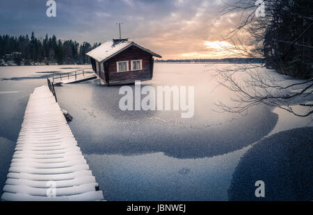 Verlassene Hütte mit Sonnenuntergang am Winterabend in Finnland Stockfoto