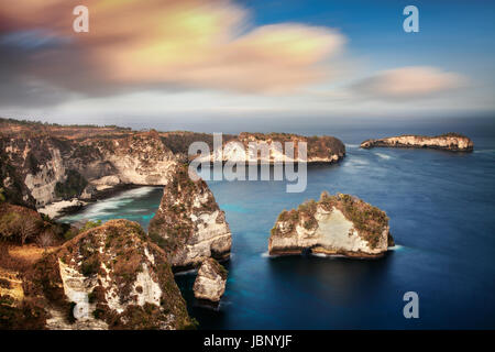 Dramatische Langzeitbelichtung von Nusa Penida Kalkstein Karst Landschaft bei Sonnenuntergang mit ungewöhnlich geformten Kalksteinfelsen. Atuh schönen weißen Sandstrand Stockfoto