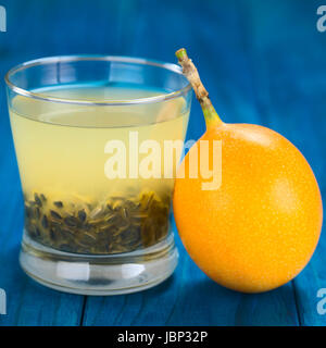 Frischer Saft gemacht süße Granadilla oder Grenadia (lat. Passiflora Ligularis) mit seinen Samen in Glas, Granadilla Obst auf der Seite (selektiven Fokus, Fokus auf dem vorderen Rand des Glases und auf der Vorderseite die Granadilla) Stockfoto