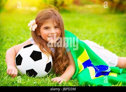 Junge fröhlich Fußballfan liegend auf frischen grünen Rasen mit Ball und große Brasilien Fahne, glücklich Unterstützer der brasilianischen Fußball-Nationalmannschaft Stockfoto