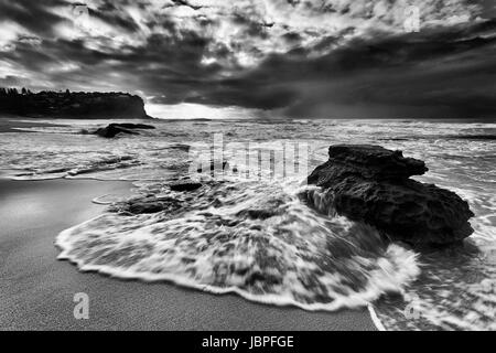 Schnell fließende Flutwelle überflutet Sandstein Felsen am Strand von Sydney Nord-Sandstrände der Bungan bei Sonnenaufgang bei stürmischem Wetter. Stockfoto