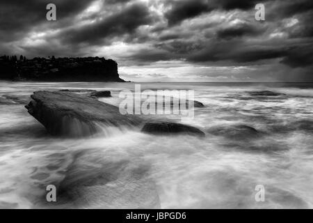 Dramatische stürmischen Wetterbedingungen am Sydney Küste des Pazifik Aroudn Bungan Strand mit getauchten Felsbrocken überflogen von sanften Wellen in schwarz-weiß-co Stockfoto