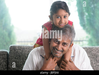 Glückliche indische Familie zu Hause. Asiatischen Vater piggyback-Tochter auf dem Sofa sitzen. Eltern und Kind indoor Lebensstil. Stockfoto