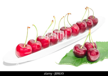 Große dunkle rote Reife Kirsche Beere Zeile auf lange weiße Schale und frische grüne Blätter isoliert angeordnet Stockfoto