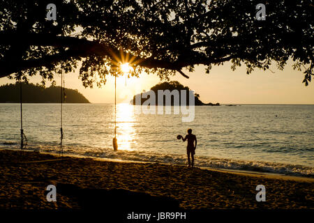 Ein junger Mann springt einen Ball bei Sonnenuntergang am Teluk Nipah Strand Insel Pangkor (Pulau Pangkor), vor der Küste von West-Malaysia. Stockfoto