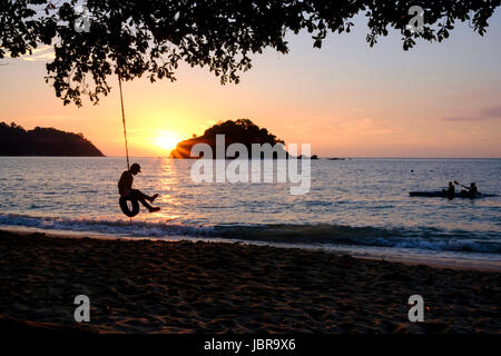 Ein junger Mann auf einem Reifen Swin und Kanu im Sonnenuntergang, Teluk Nipah Strand Pangkor Island (Pulau Pangkor), vor der Küste von West-Malaysia. Stockfoto