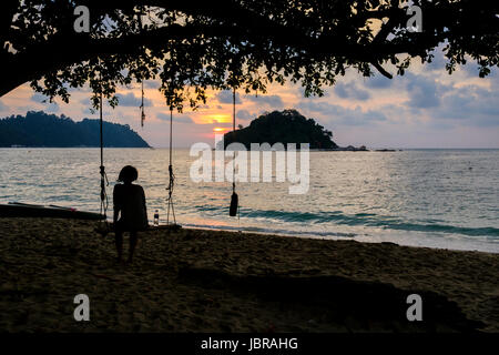 Eine Frau wacht Sonnenuntergang sitzen auf einer Schaukel, Teluk Nipah Strand Pangkor Island (Pulau Pangkor), Malaysia. Stockfoto
