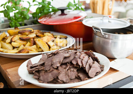 Nahaufnahme der Platten von gekochtem Fleisch und dicken Stil Pommes Frites auf Tisch bereit zum Servieren bei Dinner-party Stockfoto