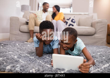 Lachende Kinder mit digital-Tablette während die Eltern zu Hause auf Sofa Standortwahl Stockfoto