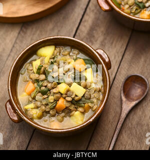 Vegetarische Suppe aus Linsen, Spinat, Kartoffeln, Karotten und Zwiebeln serviert in dunkel braun Schüssel (selektiven Fokus, Fokus ein Drittel in die Suppe) Stockfoto