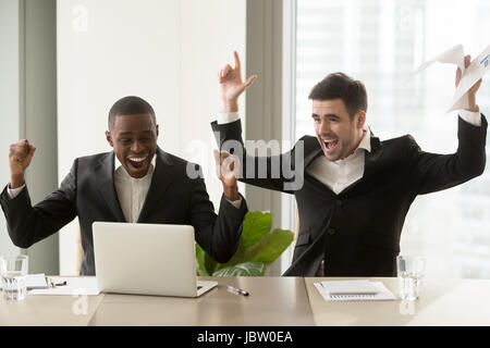 Zwei glückliche Geschäftsleute in Anzügen, die Hände in der Nähe von Laptop, multikulturellen Unternehmensgruppe feiern Sieg, stock trading-Erfolg, beeindruckende achievemen Stockfoto