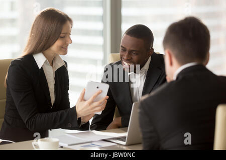 Junge kaukasischen Geschäftsfrau zeigt an afrikanischen Kollegen etwas komisch auf Tablet während der Pause, Treffen mit Videokonferenz app for Business, soc Stockfoto