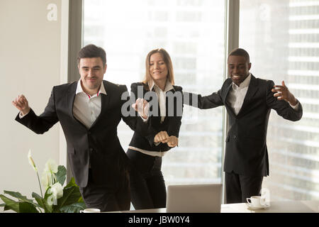 Aufgeregt afrikanischen und kaukasischen Mitarbeiter im Büro tanzen, party Personal, positive multiethnischen Team zufrieden mit Ergebnis, profitables Zuschlag, gro Stockfoto