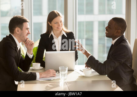 Gruppe von attraktiven multirassische lachende Geschäftsleute reden und scherzen am Schreibtisch in hellen modernen Büro, freundliche multiethnischen Business-team Stockfoto