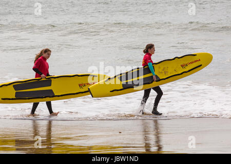 zwei weibliche Bournemouth Rettungsschwimmer Leben Schlitten Surfbretter in das Meer am Strand von Bournemouth, Dorset im Juni zu tragen Stockfoto