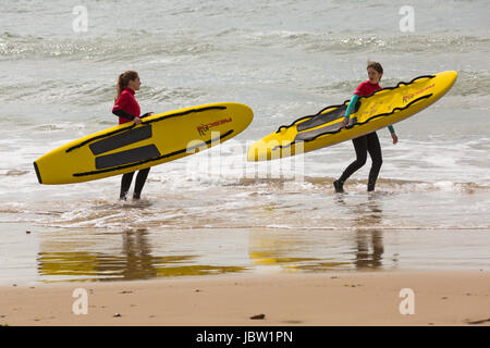 zwei weibliche Bournemouth Rettungsschwimmer Leben Schlitten Surfbretter in das Meer am Strand von Bournemouth, Dorset im Juni zu tragen Stockfoto