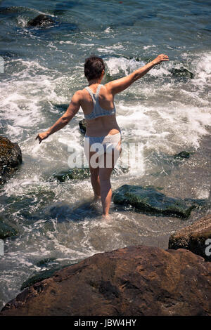 Applying Frau zu Fuß in Wasser auf felsigen Strand. Stockfoto