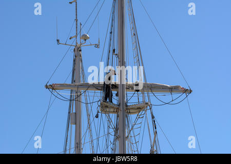 Ein weiblicher Seemann arbeitet an der Takelage hoch oben am Mast Yacht im Hafen von Weymouth, Weymouth, Dorset, England, UK Stockfoto