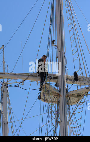 Ein weiblicher Seemann arbeitet an der Takelage hoch oben am Mast Yacht im Hafen von Weymouth, Weymouth, Dorset, England, UK Stockfoto