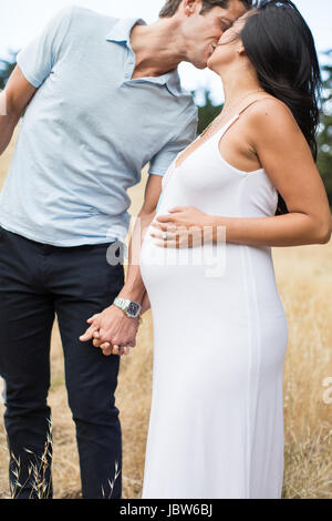 Schwangere Frau und reifer Mann, Hand in Hand, küssen, im freien Stockfoto