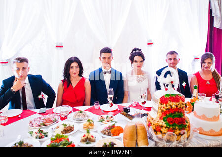 Hochzeitspaar und Brautjungfern mit Trauzeugen sitzen an einem Tisch voller leckere Gerichte. Stockfoto